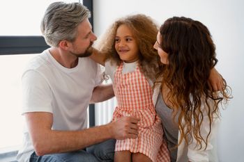 Three people smiling and embracing on a couch in a bright room