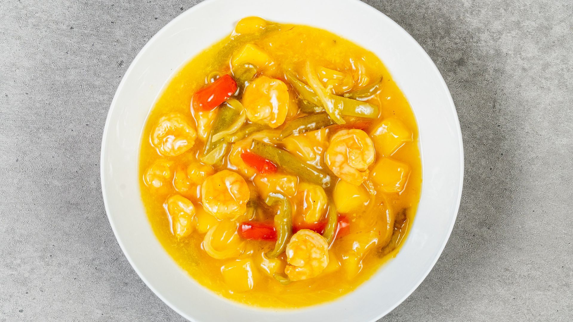 White bowl of yellow chicken stew with potatoes and red peppers on a gray surface