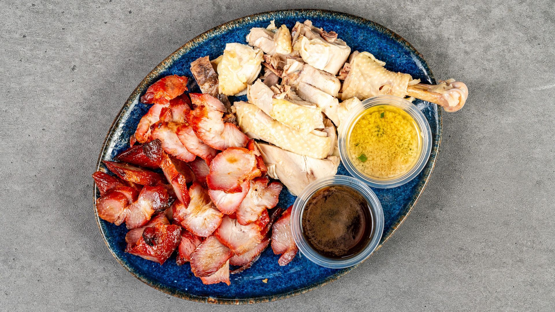 Blue plate with assorted grilled meats and two dipping sauces on a gray table