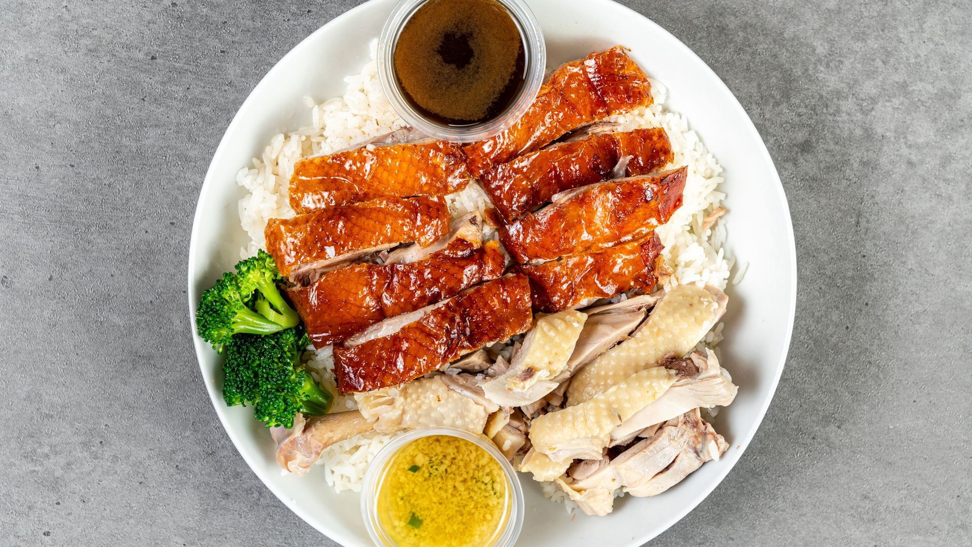 Plate of roasted meat with rice, broccoli, egg, and sauce on a gray table