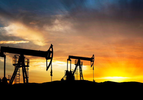 Silhouette of oil pump jacks against a vibrant sunset sky.
