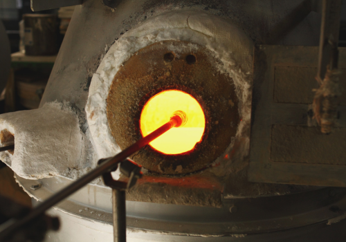 Molten glass on a rod inside a furnace; glowing orange, with insulating materials surrounding the opening.
