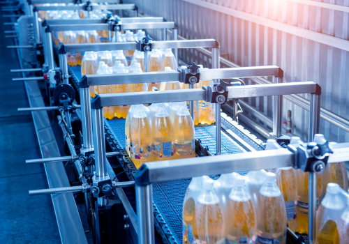 Bottles of yellow liquid packaged on a conveyor belt in a factory setting.