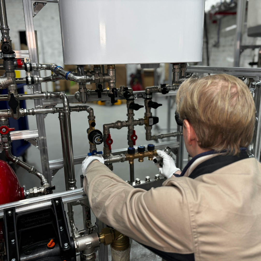 A technician wearing white gloves adjusting metal pipes and valves on a complex industrial plumbing system.