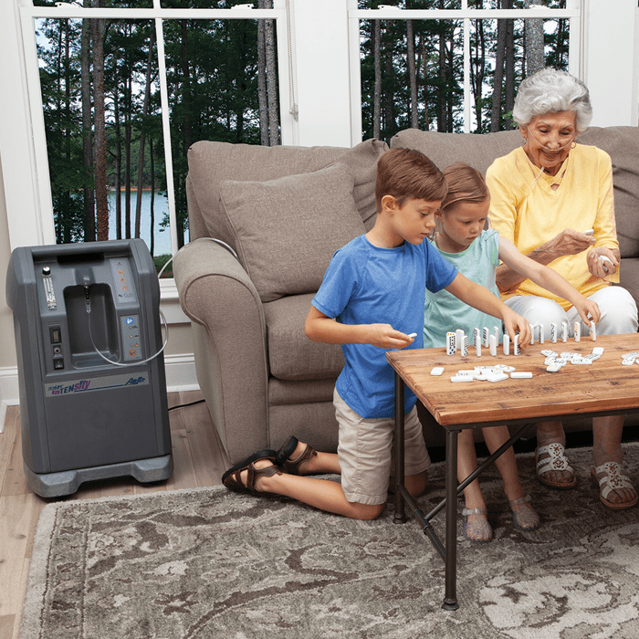 A woman and two children playing dominoes near an oxygen concentrator indoors.