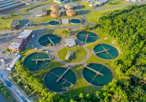 Aerial view of a wastewater treatment plant with multiple circular basins and surrounding infrastructure.