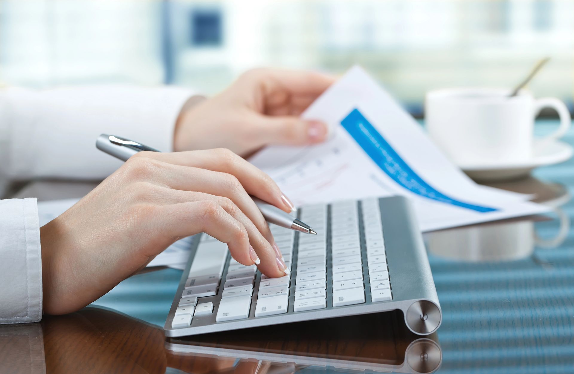 A person is typing on a keyboard while holding a pen