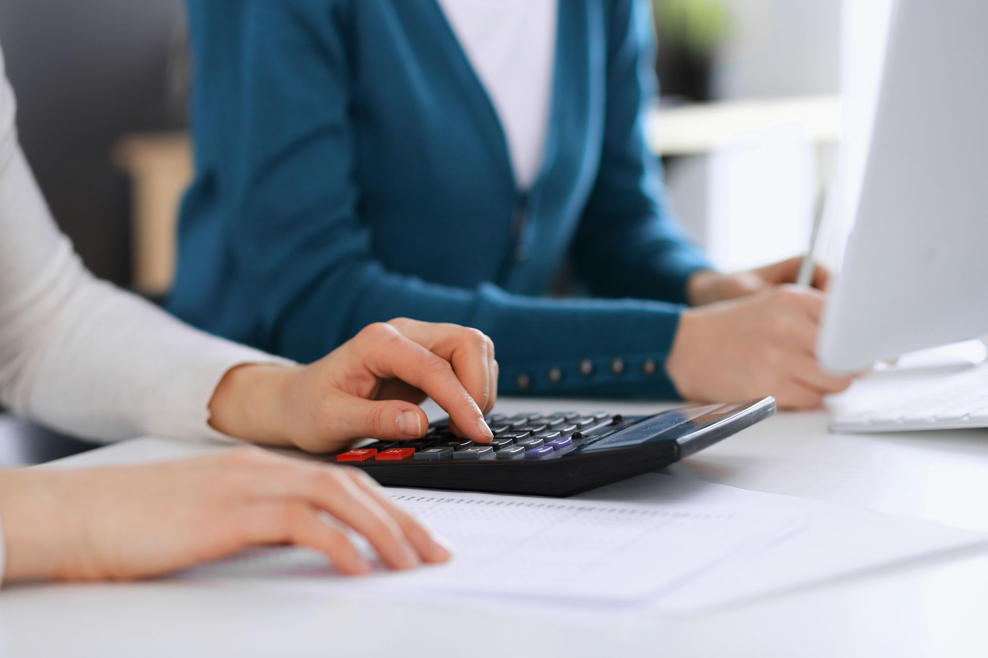 Two women are sitting at a table using a calculator.