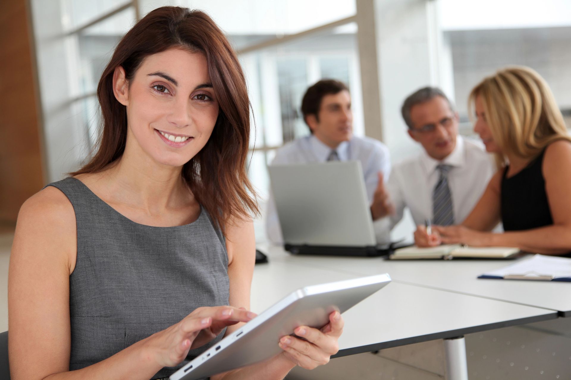 A woman is holding a tablet in front of a group of people.