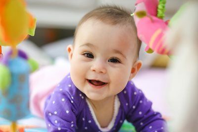 Smiling baby in a purple polka-dot outfit on a colorful play mat