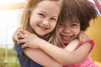 Two smiling children hugging each other outdoors in bright sunlight