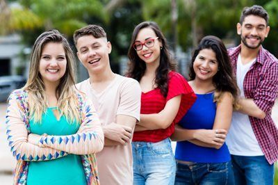Five smiling friends standing outdoors with arms crossed, wearing colorful casual clothes.