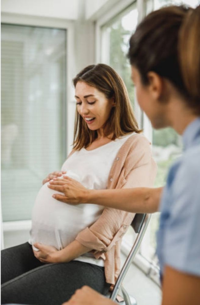 Pregnant woman smiling while having her belly examined by a clinician in a bright clinic