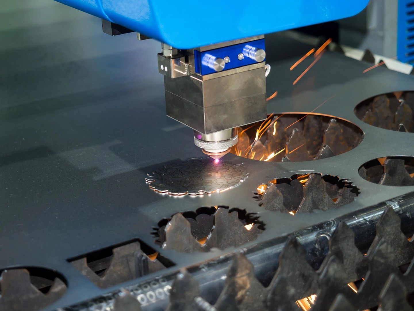 Un laser cutter pratica dei fori in una lamiera, con scintille che volano.