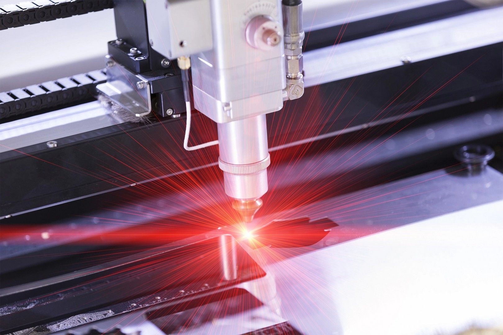 Taglierina laser in azione: emette un raggio rosso brillante e taglia una superficie scura.
