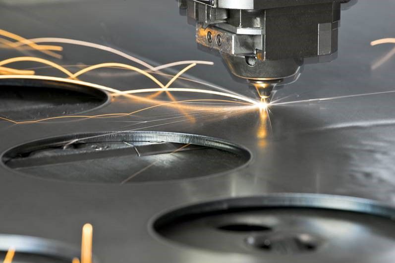 Macchina per il taglio laser in azione: le scintille volano e creano fori in una lamiera.