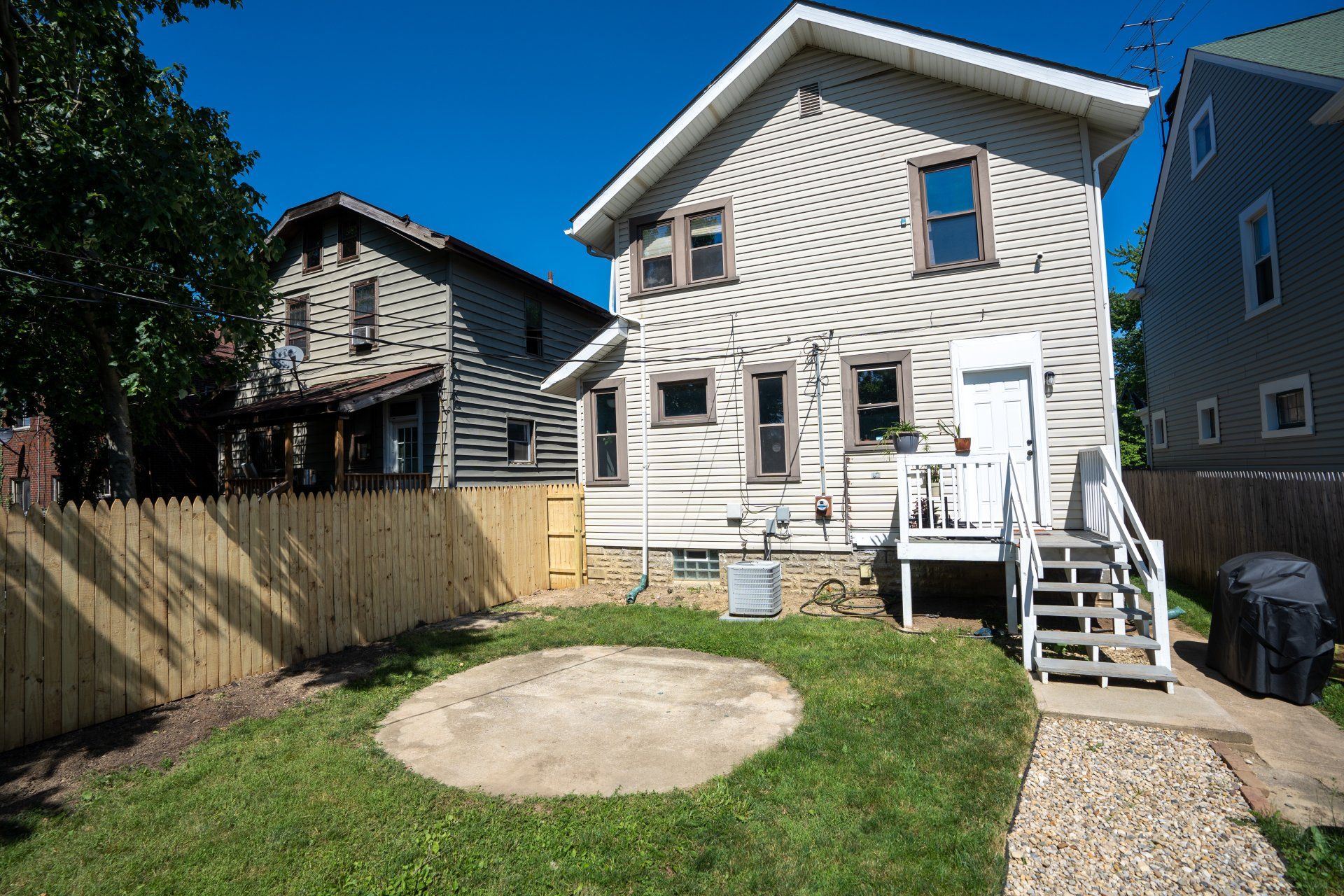 Backyard with white two-story house, wooden fence, small lawn, and concrete patio circle