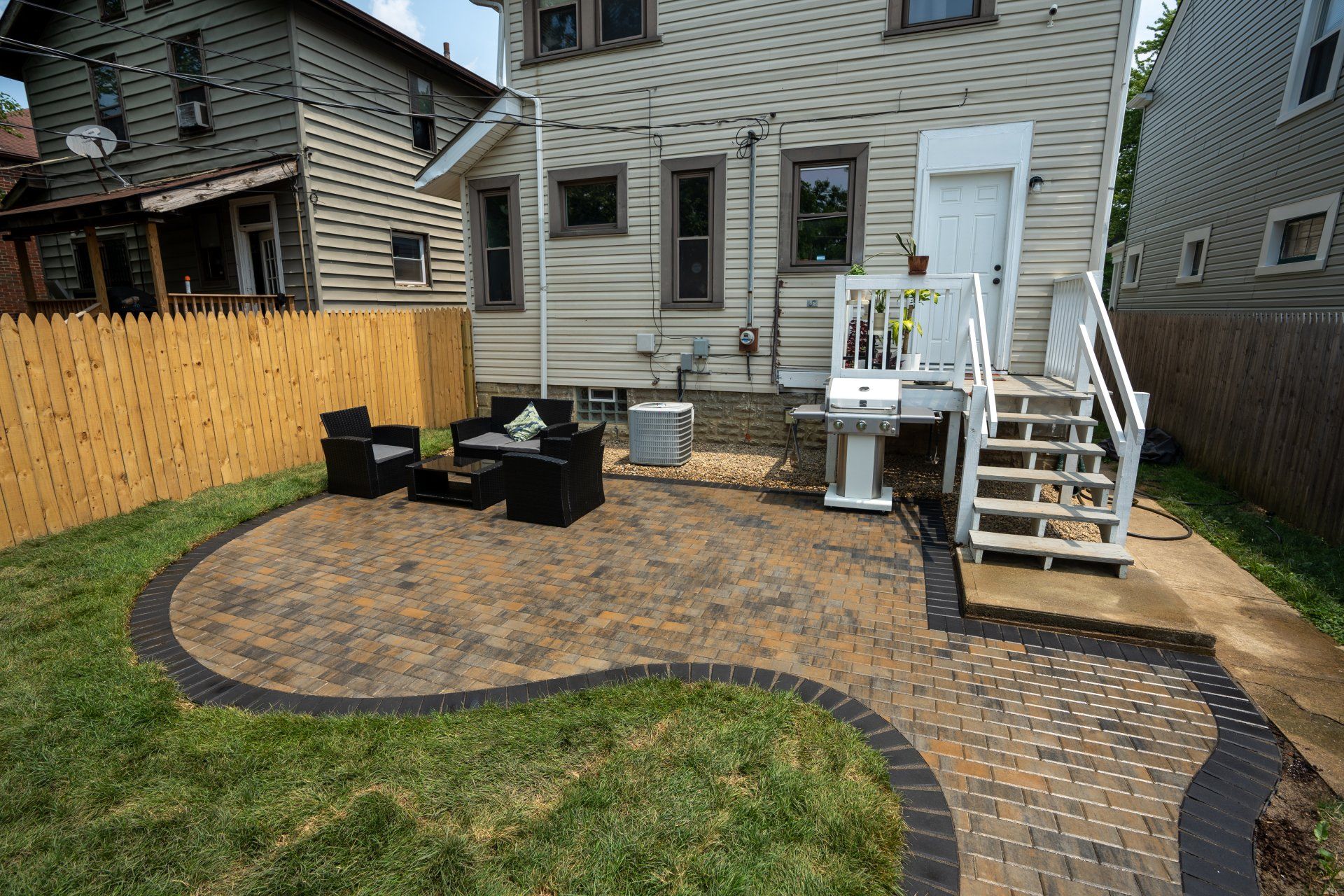 Backyard patio with winding paver path, black seating, and white stairs beside a house