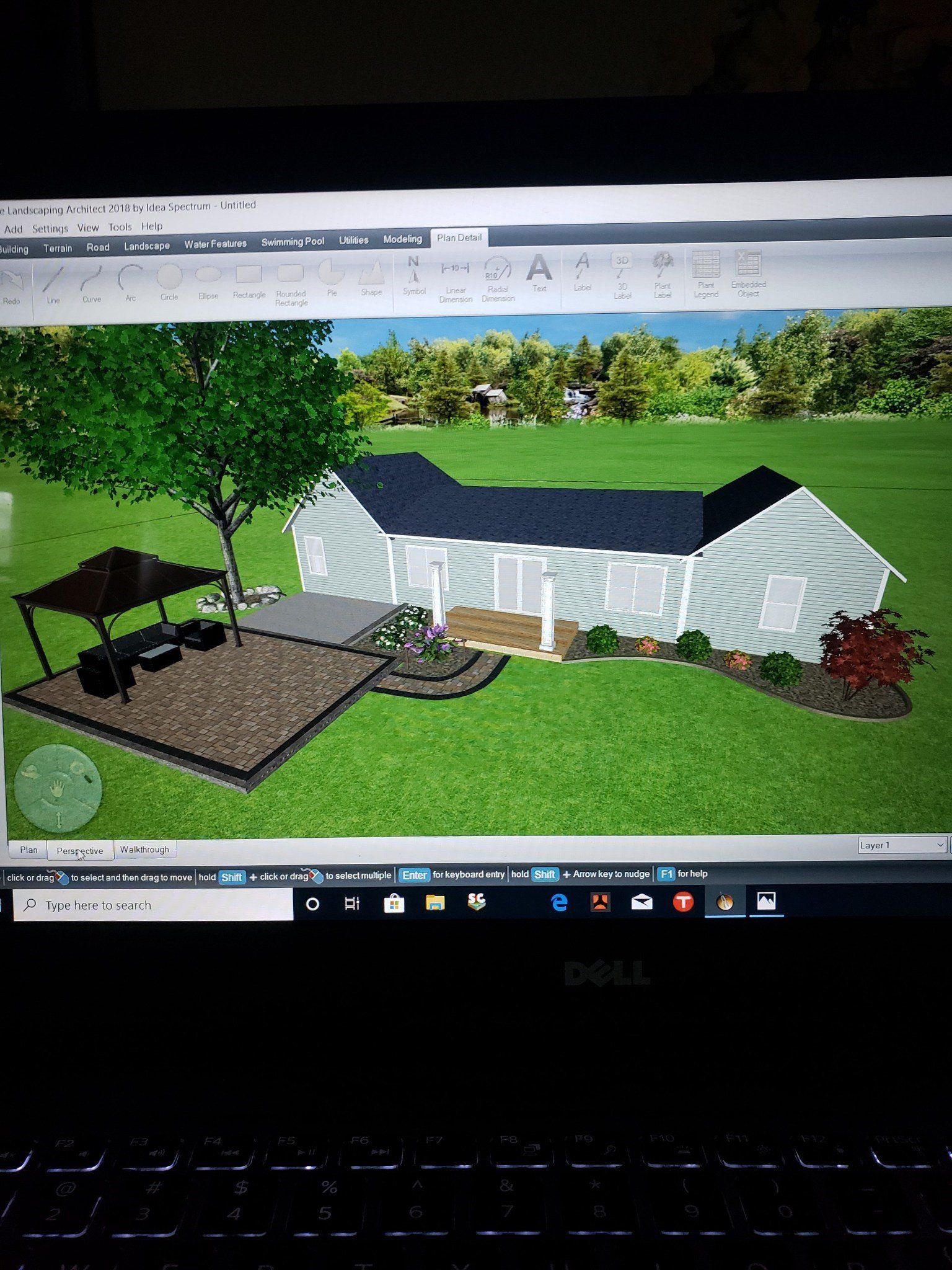 Landscape design render of a white house with black roof, garden beds, and trees on a computer screen