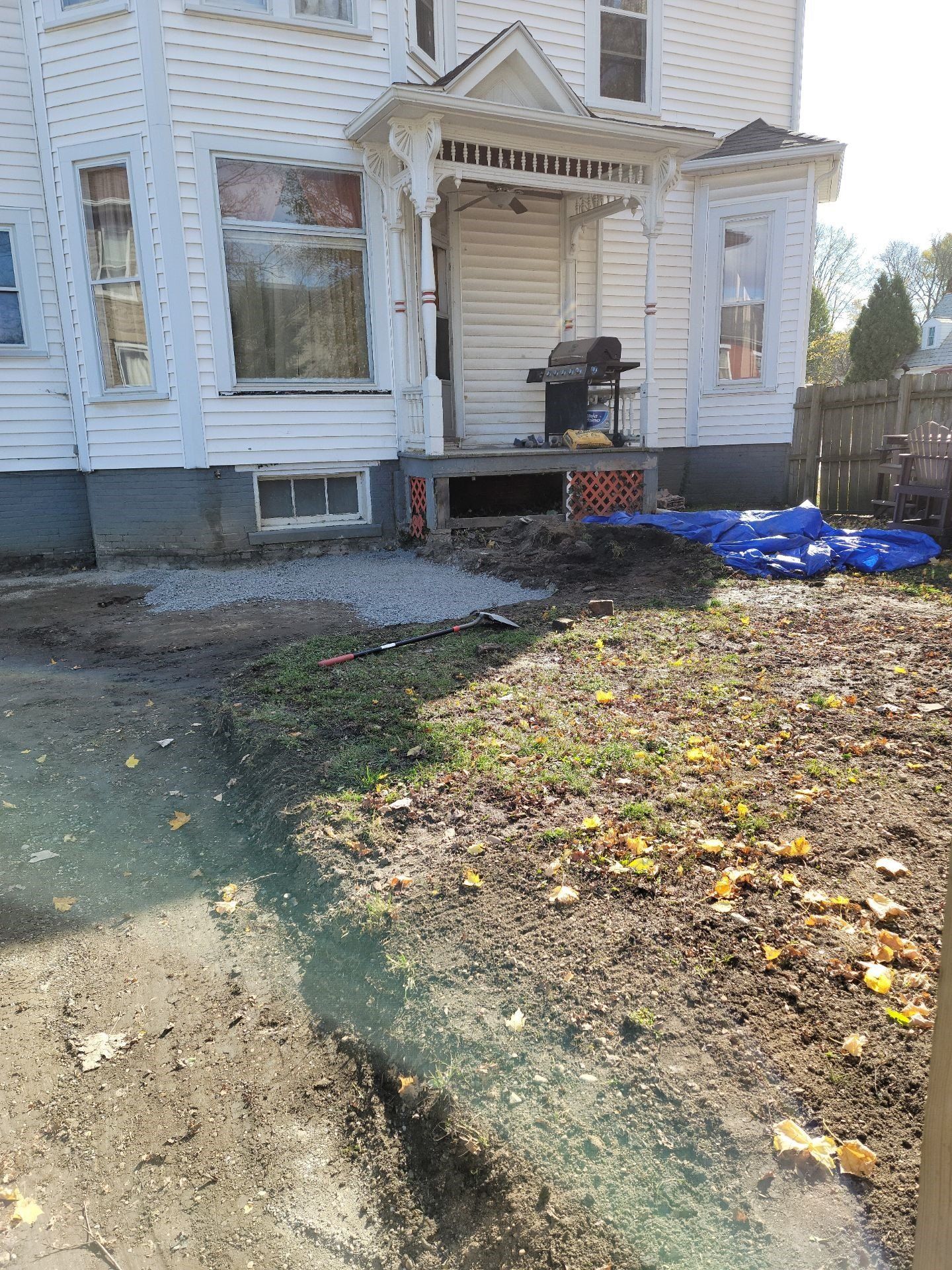 Dilapidated white house with damaged porch, debris, and blue tarp in front yard