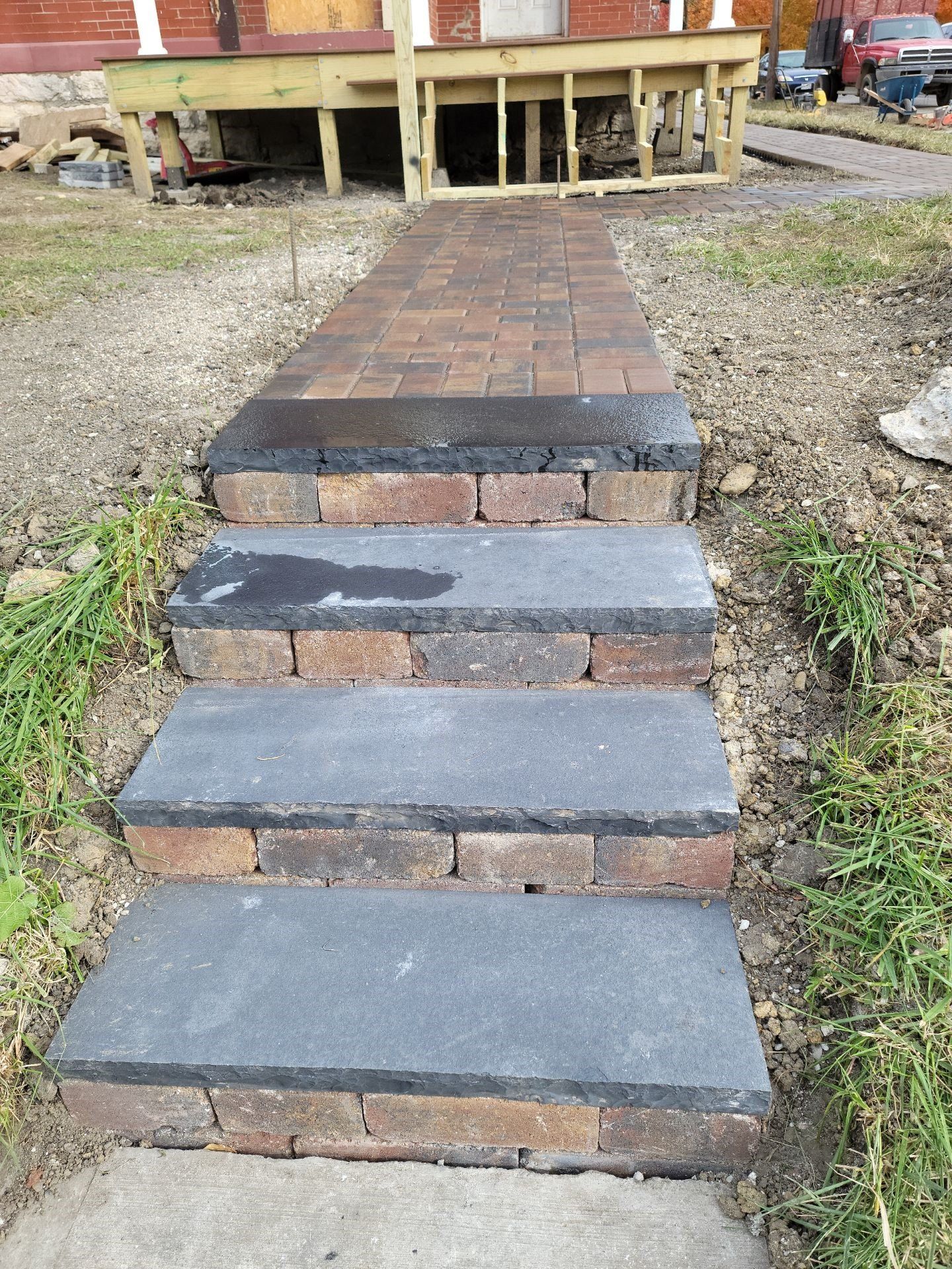 Stone steps leading up to a brick walkway and porch beside a house, with gravel and grass edges