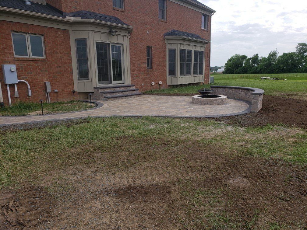 Brick house with curved stone patio and fire pit overlooking a grassy backyard and open field