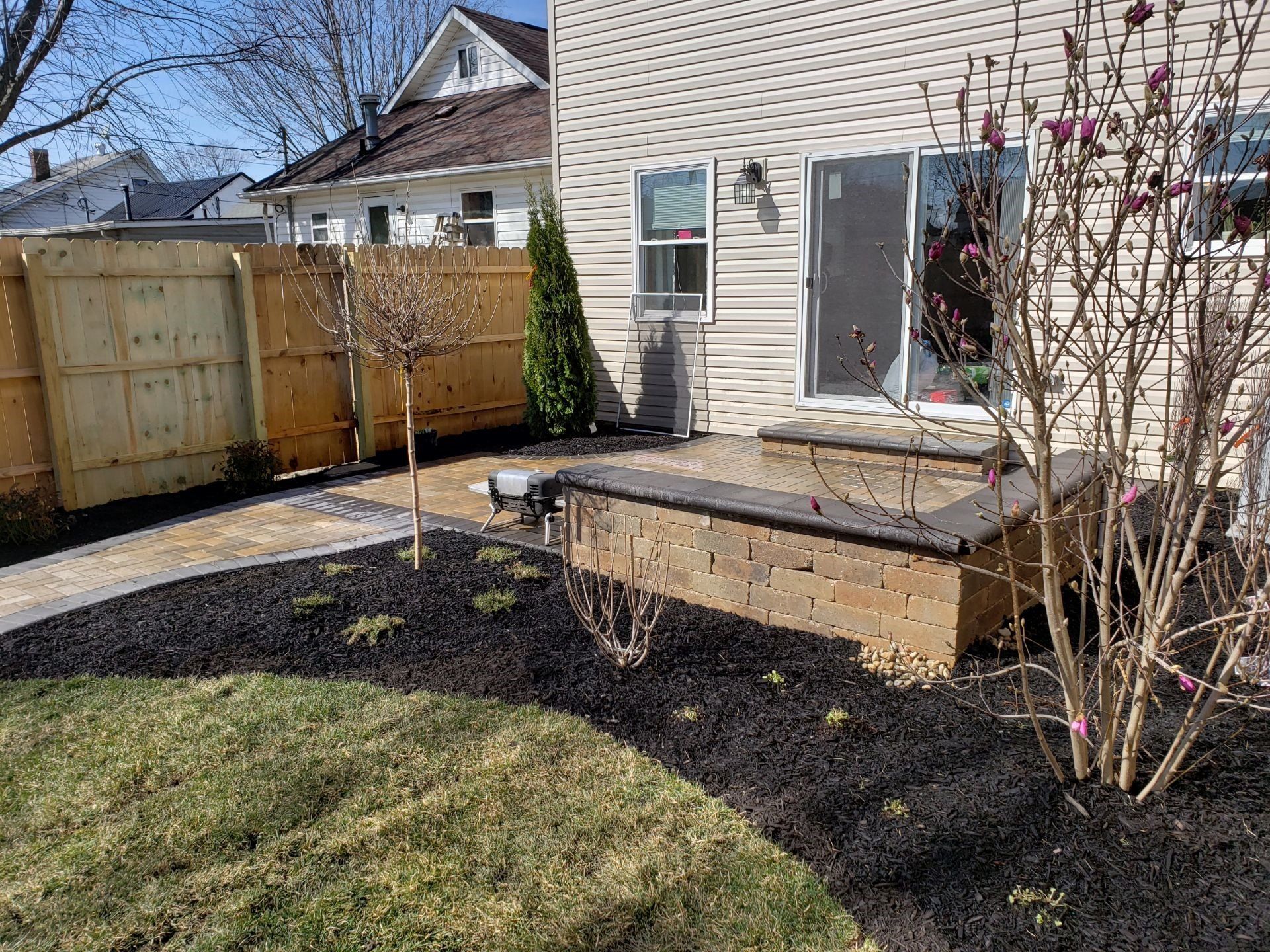 Backyard patio with a wooden bench, black mulch bed, fence, and beige house exterior