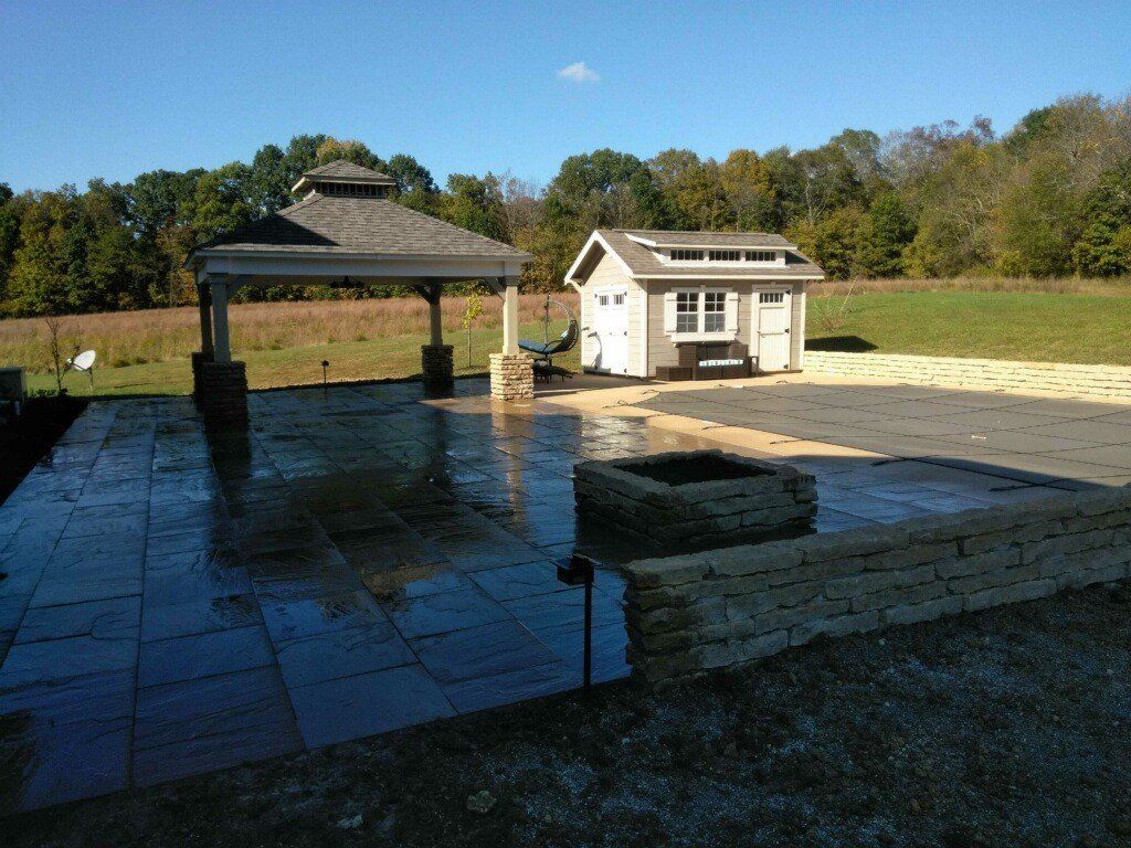 Outdoor stone patio with gazebo and small white shed under a clear blue sky