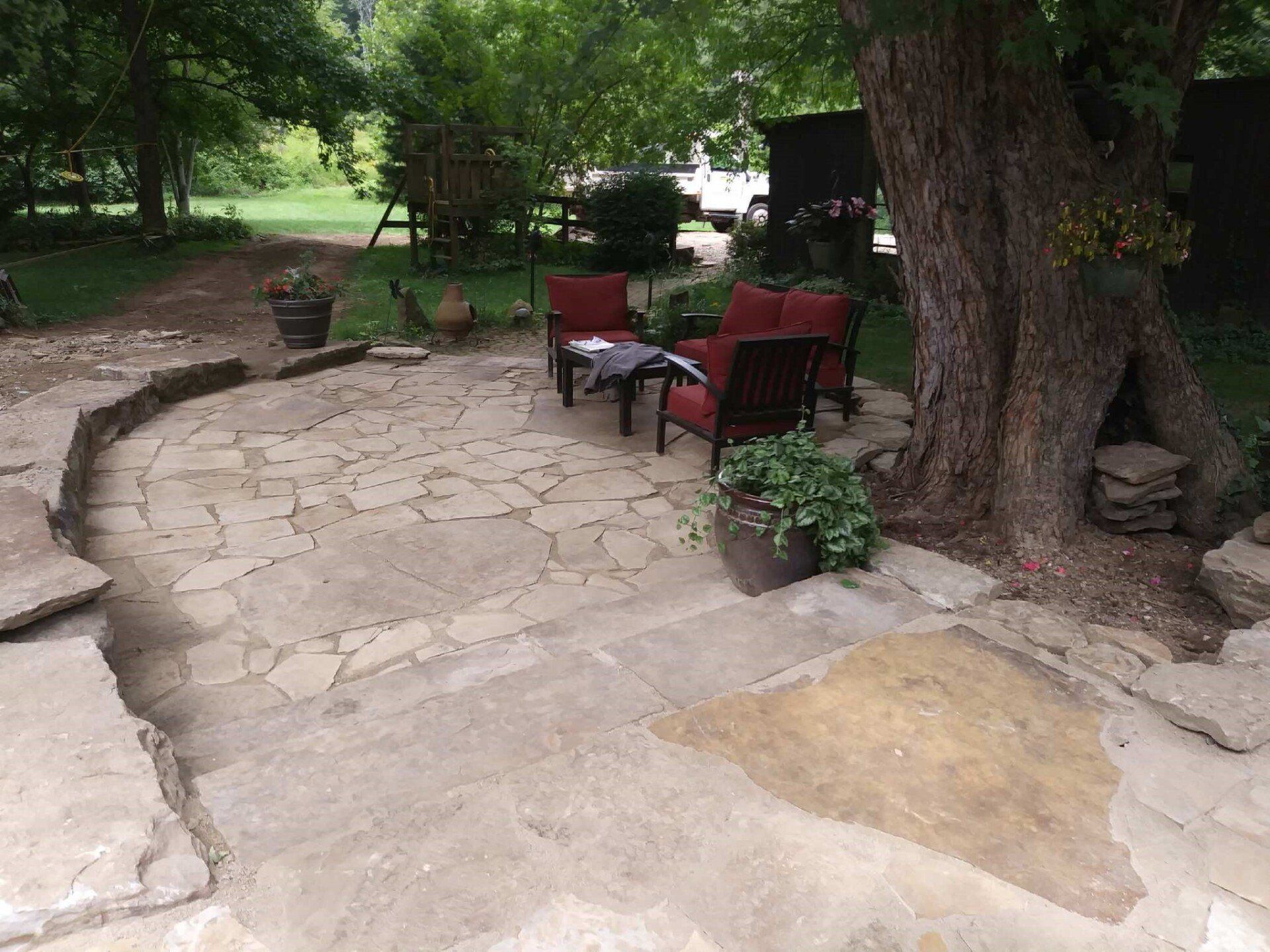 Stone patio with red chairs and a table under trees in a shady garden