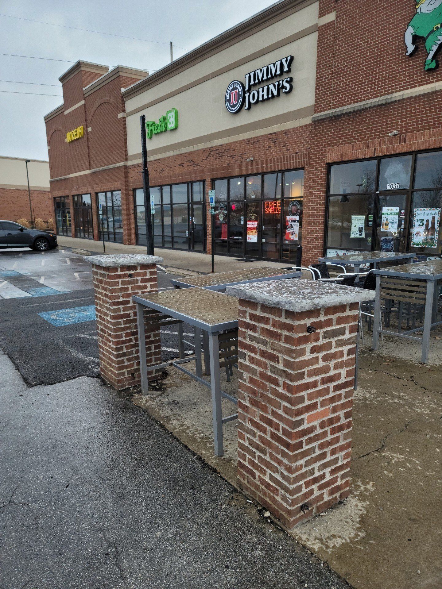 Brick storefronts of Jersey Mike’s and Panda Express with a wet sidewalk and outdoor seating area