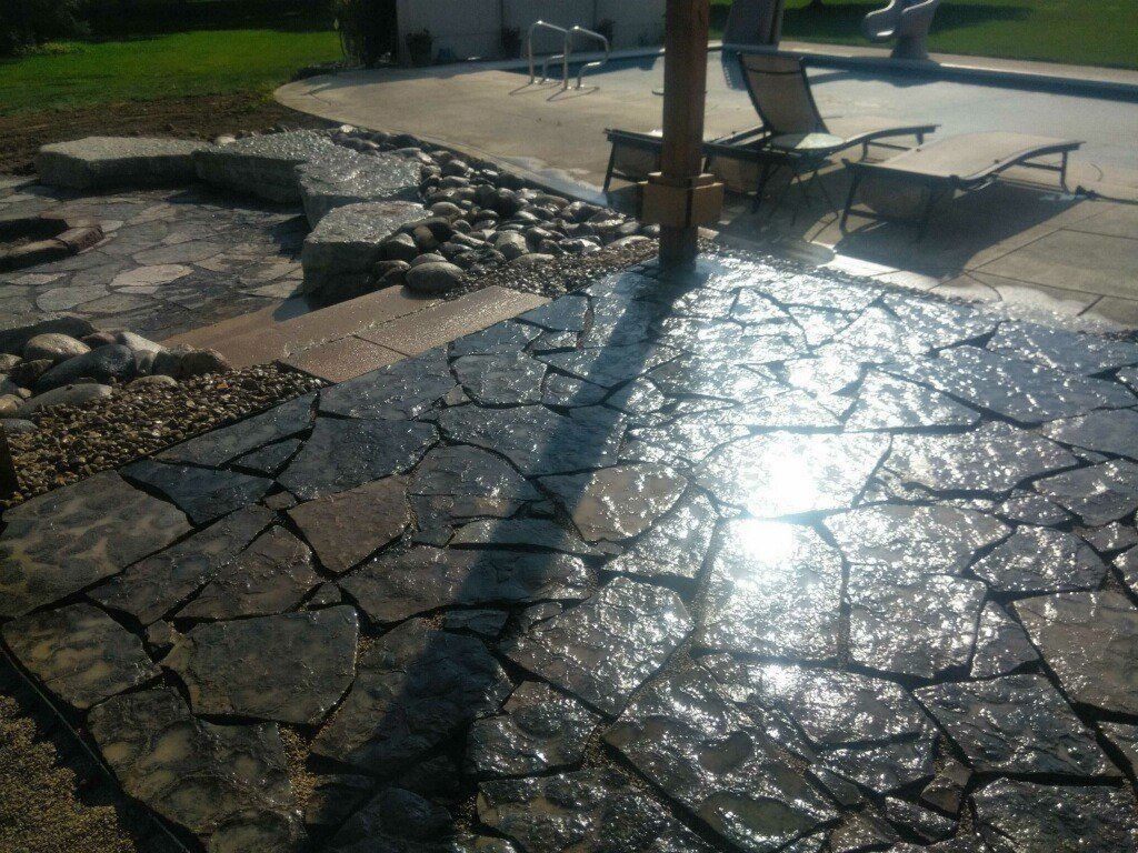Sunlit stone patio with lounge chairs and strong reflections on wet paving stones