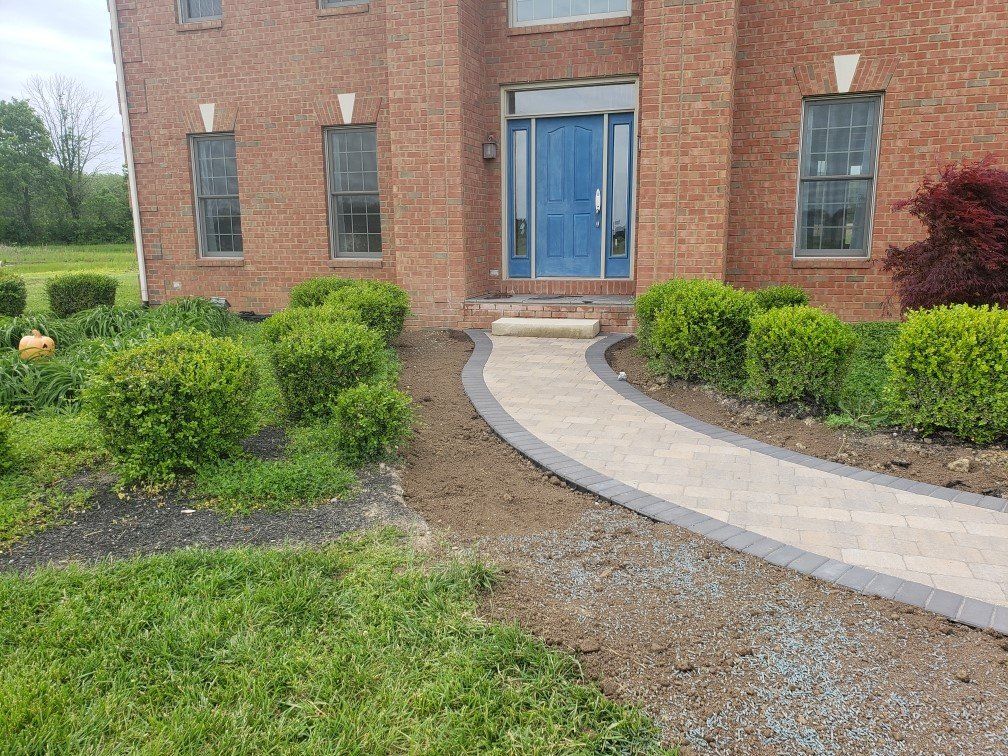 Brick building entrance with blue double doors, curved stone walkway, and trimmed shrubs in front.