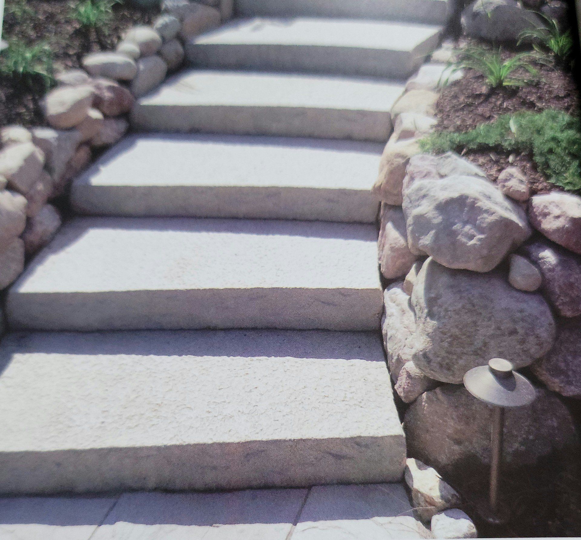 Stone steps ascending through a landscaped garden with rocks and a small path light