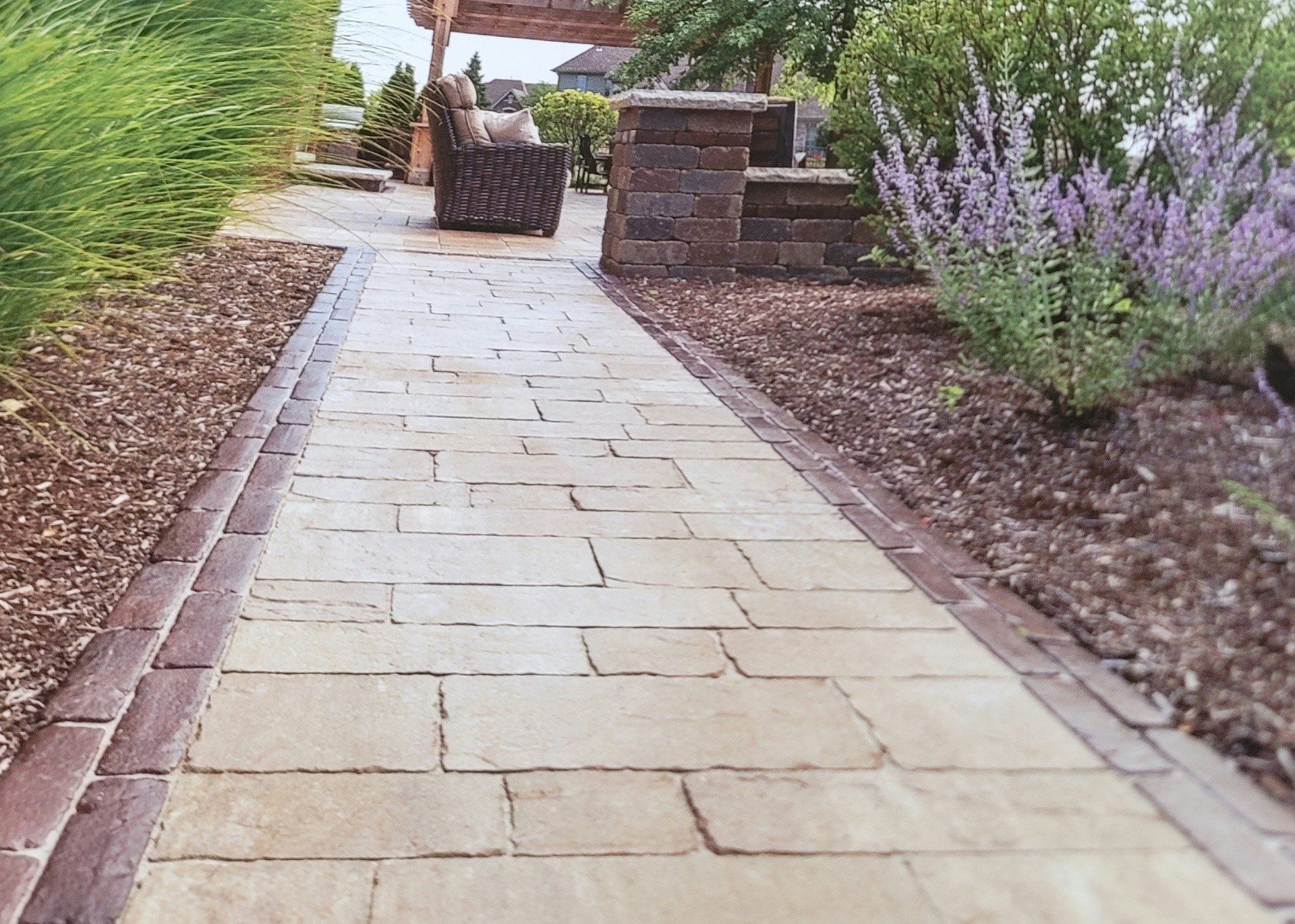 Stone garden path with brick edging, leading past purple flowers and a patio seating area