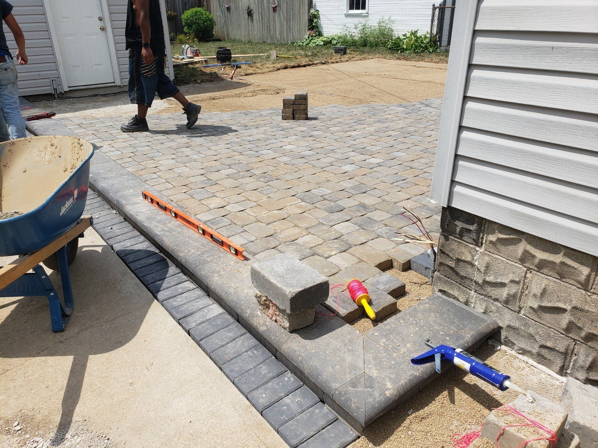 Partially built concrete patio with tools, bricks, and a person walking in the background