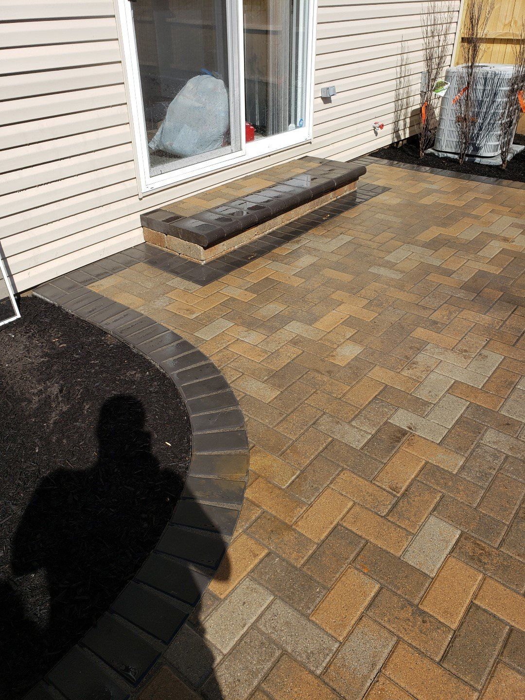 Patio with paver stones, house siding, a window, and a small wooden step bench.