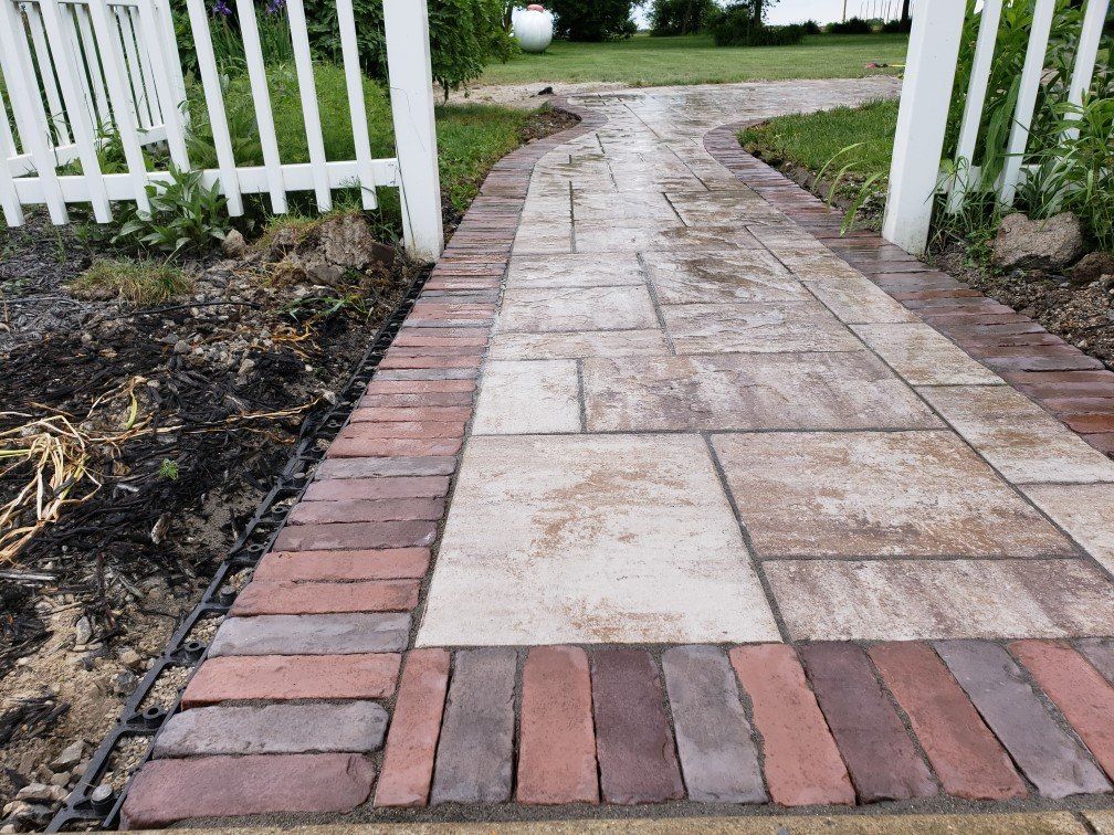 Brick and stone walkway through a white picket gate in a garden
