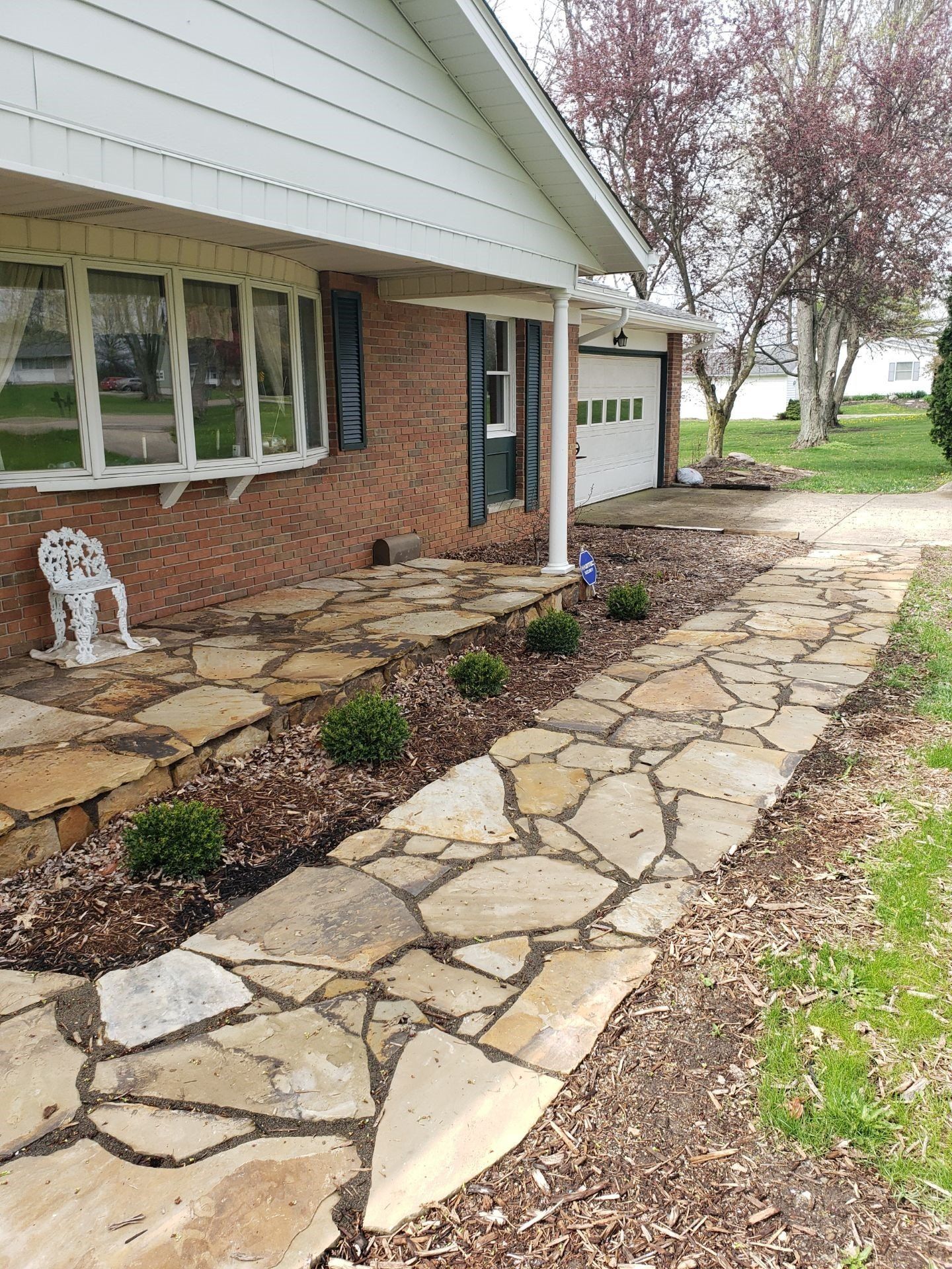 Stone walkway along a brick house with white trim and a small front garden.
