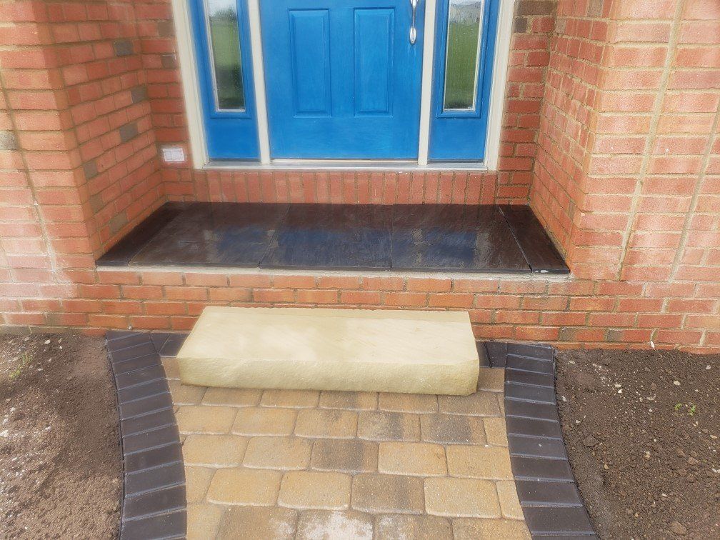 Brick house entrance with blue front door, tiled stoop, and a small ramp over the doorstep.