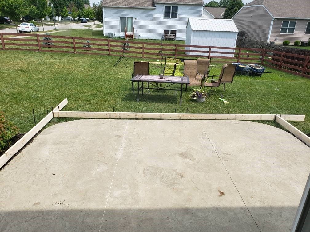 Backyard concrete patio with two tables, chairs, and a wooden fence beyond the grass