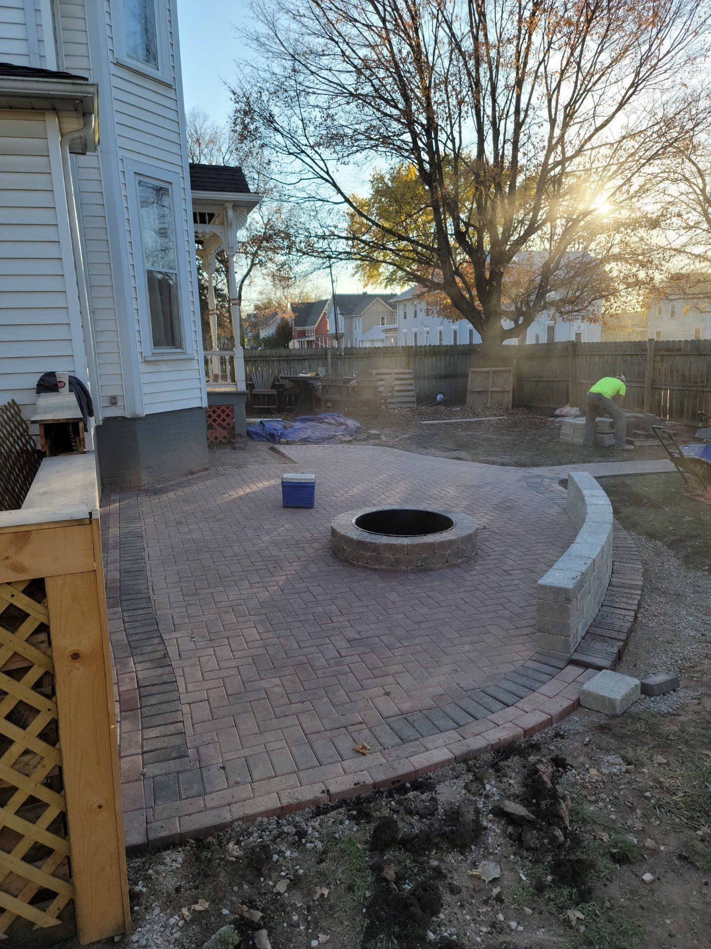 Backyard brick patio with fire pit, curved stone bench, and a house at sunset