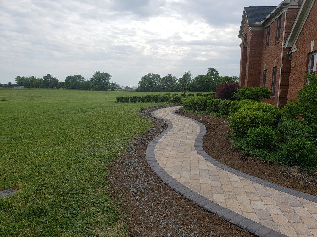 Curved brick walkway beside a brick building and green lawn under a cloudy sky