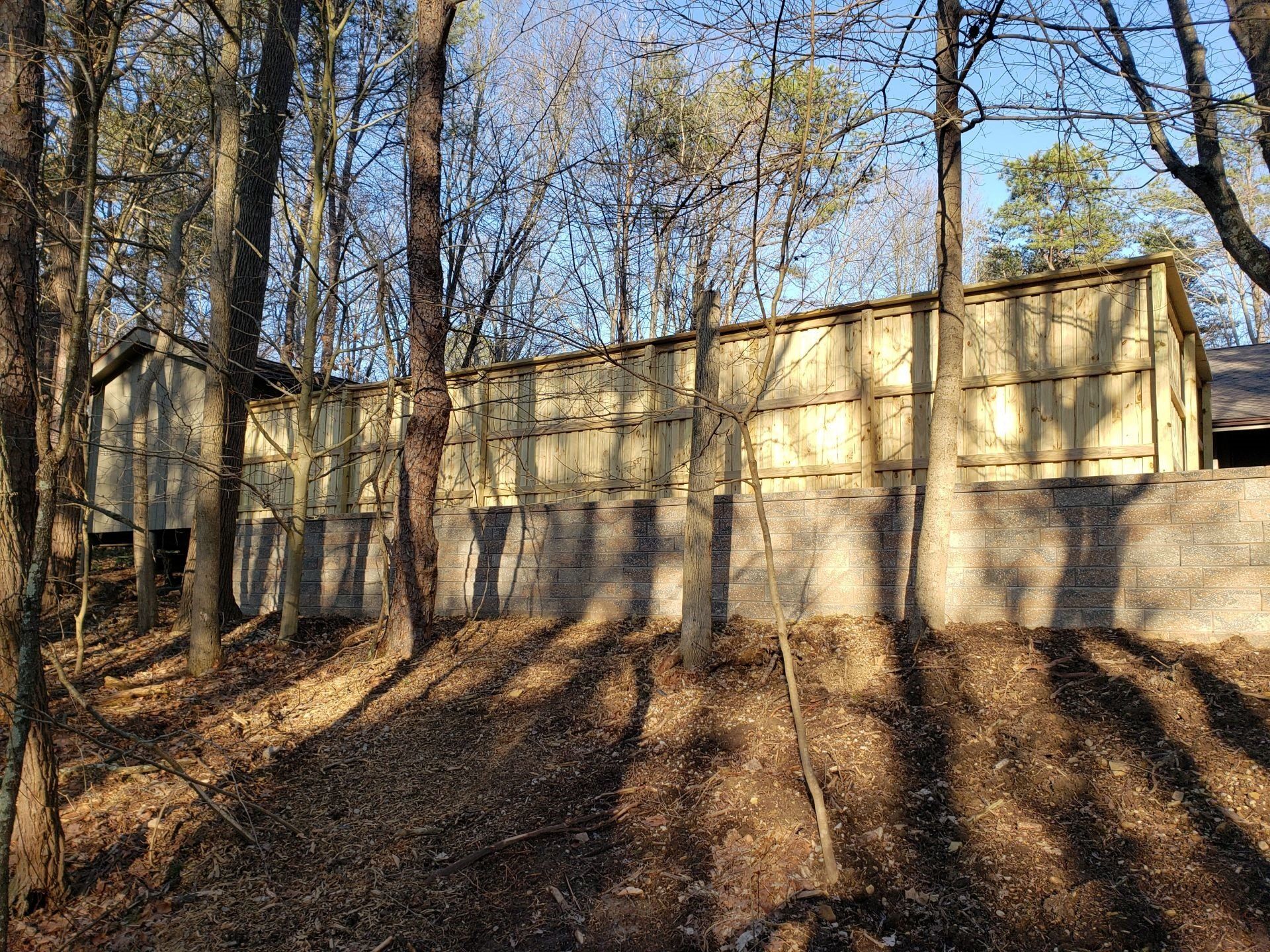 Wooden fence along a wooded hillside with long tree shadows in late afternoon light