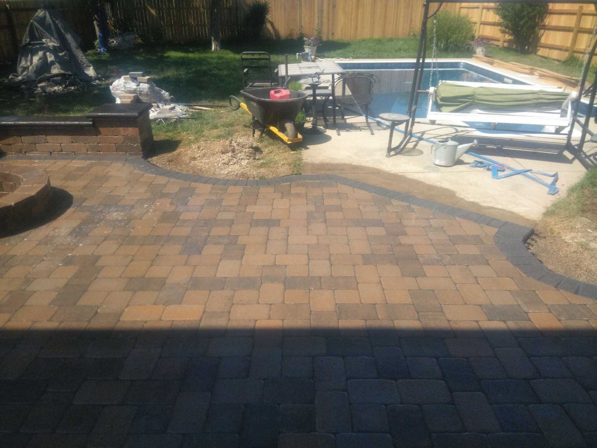 Backyard patio with paver stones, a grill, table, chairs, and folded lounge chairs near a pool.