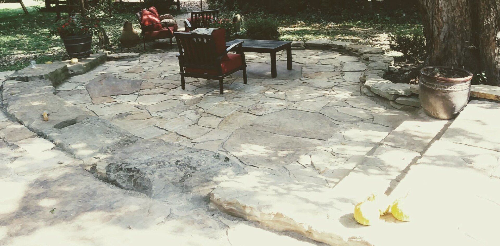 Stone patio with two chairs, a small table, and potted plants in a garden.