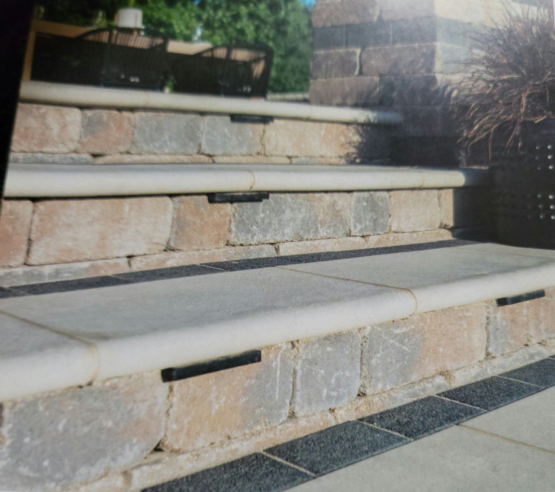 Stone steps with light-colored rounded edges leading up to a landing, beside dark shrubs and tiled paving.