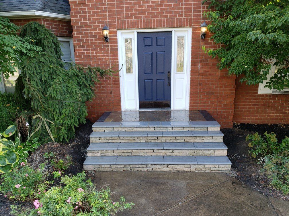 Brick house entrance with blue front door, white trim, and concrete steps leading up from a garden path