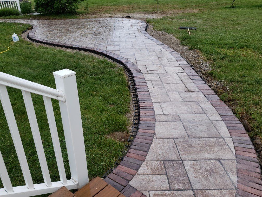 Curved stone walkway bordered by red bricks, leading through a grassy yard beside a white railing