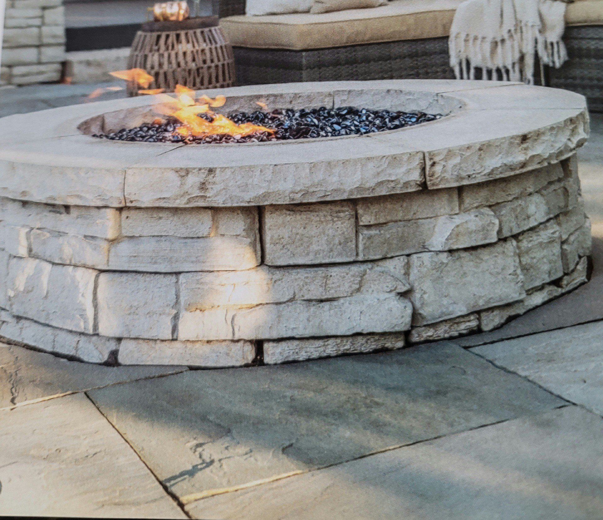 Stone outdoor fire pit with flames burning in a paved patio area