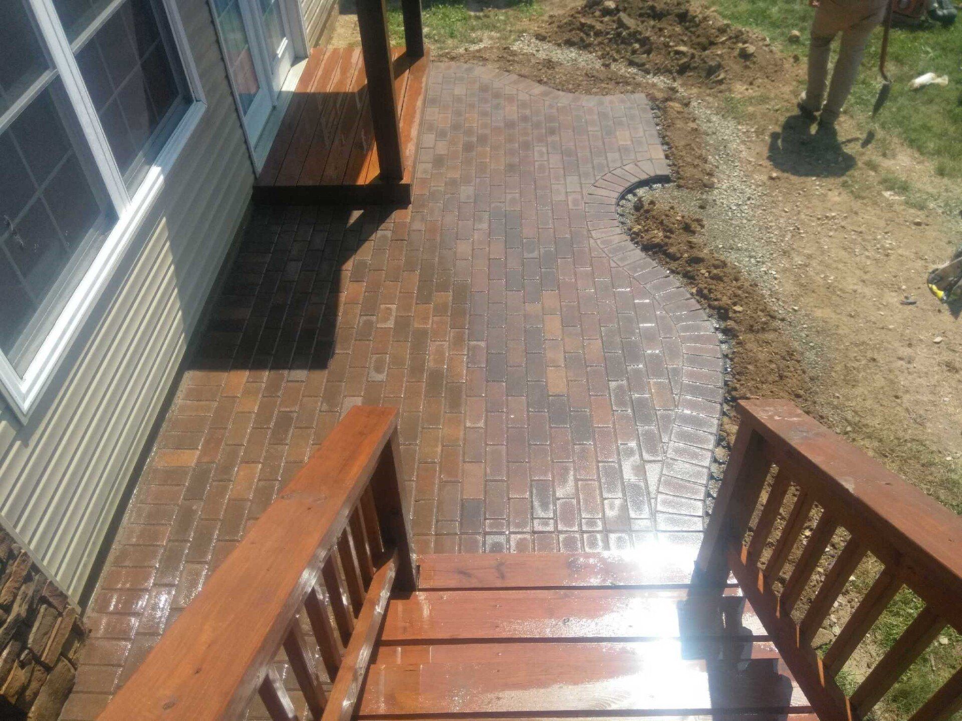 Brick patio walkway with wooden steps beside a house and a dirt yard
